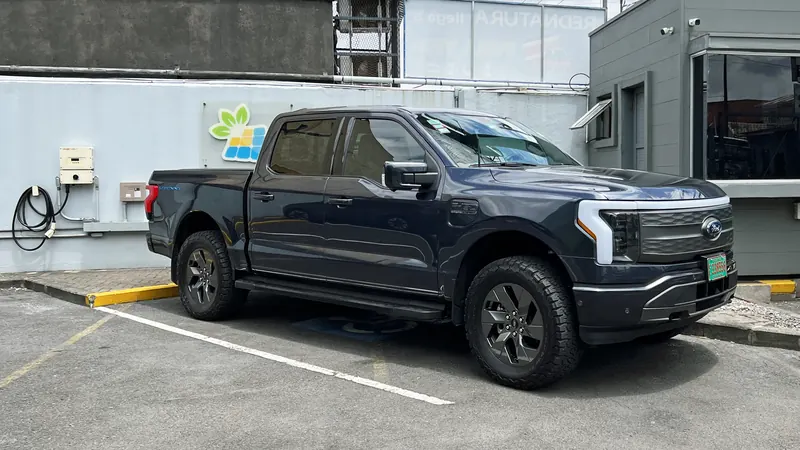 A dark Ford F-150 Lightning electric pickup truck parked beside a building