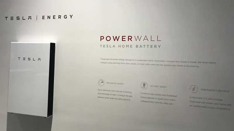 A white Tesla Powerwall 2 home battery mounted on a display wall